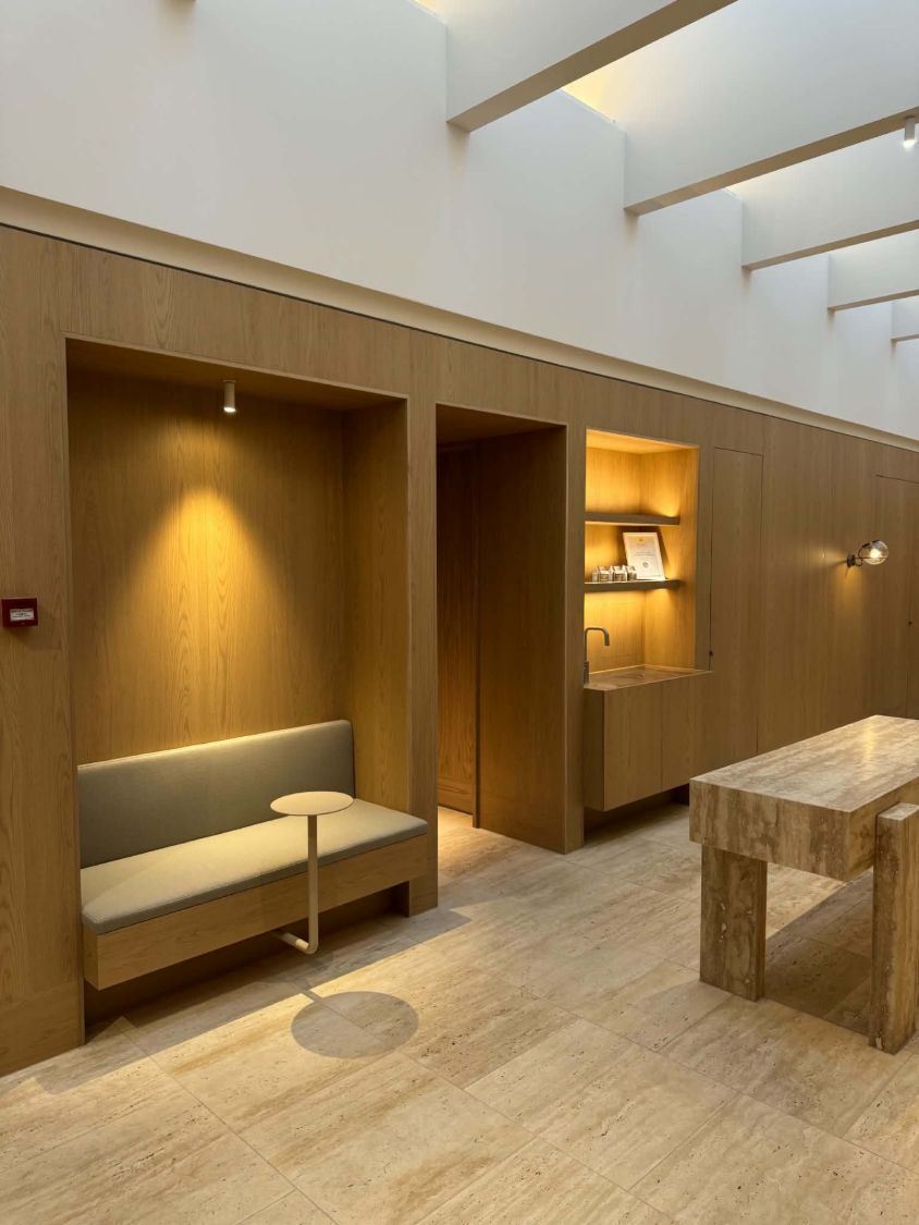 Timber-lined commercial foyer with spotlit seating niche, lit shelving and a wall light