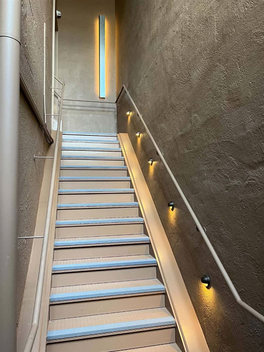 Commercial stairwell with step lights along the wall and a tall backlit feature panel at the top